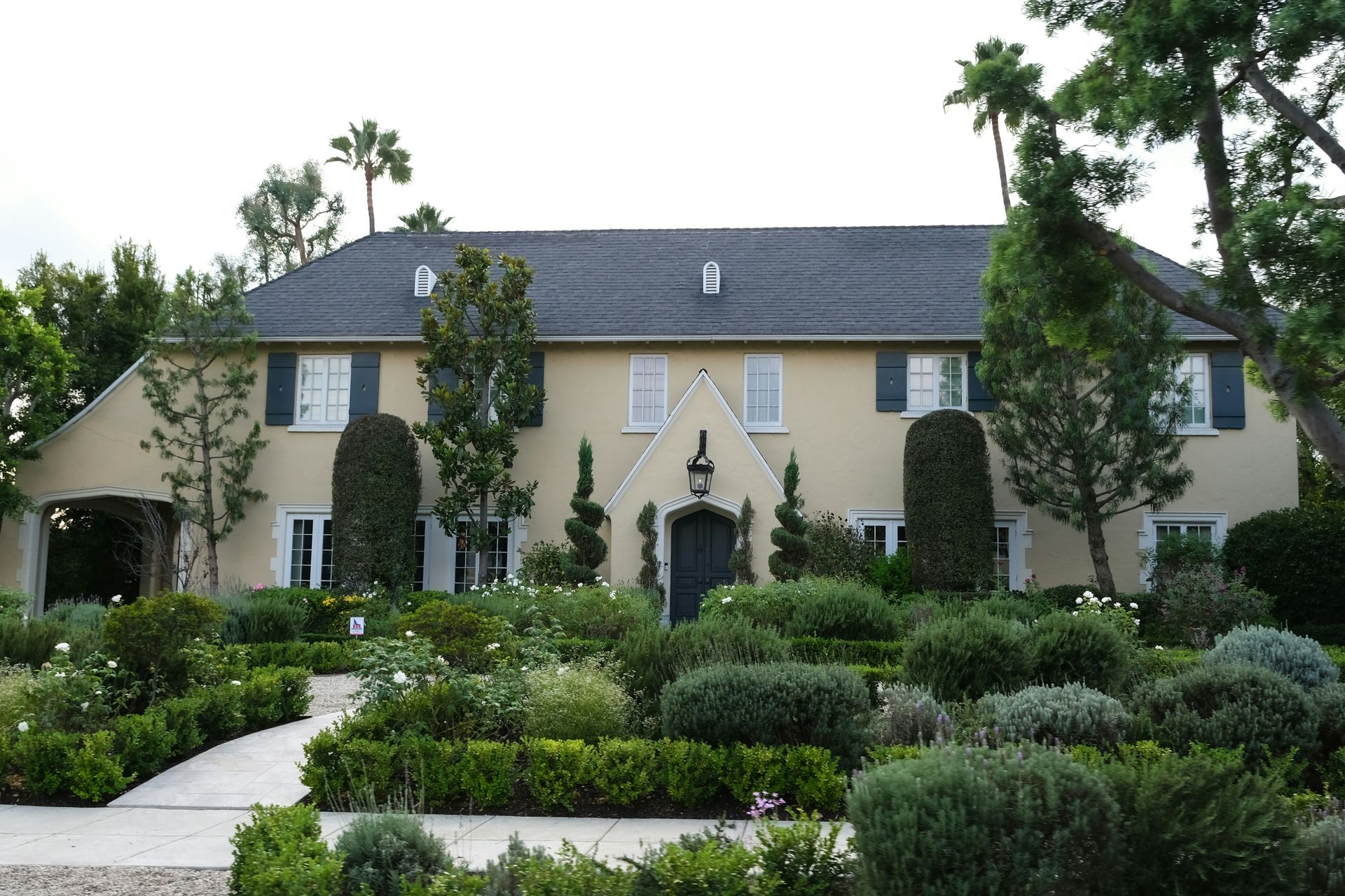 A large tan house with manicured gardens and palm trees